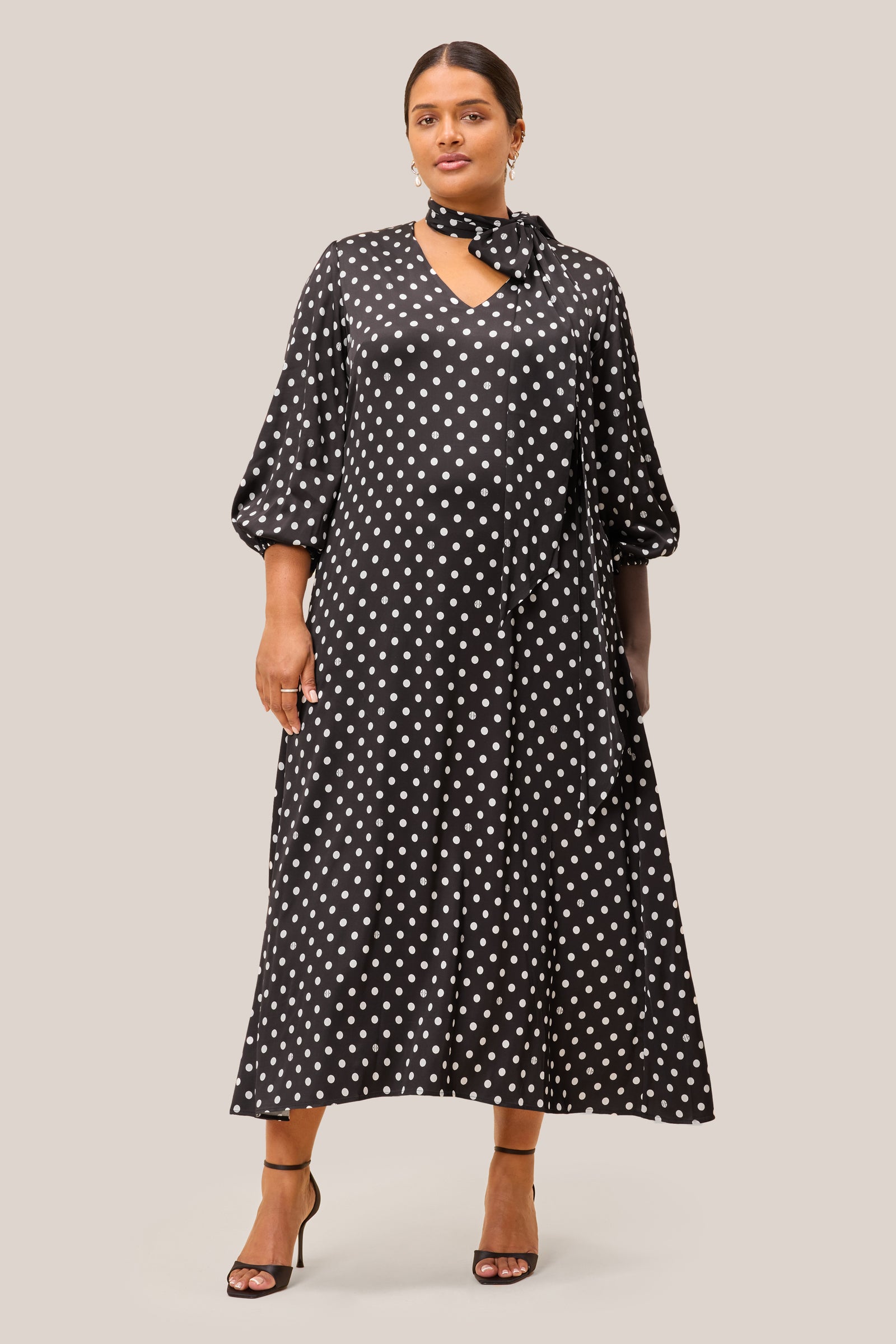 Model wearing plussize black polka dot midi dress styled for weddings or elegant daywear.