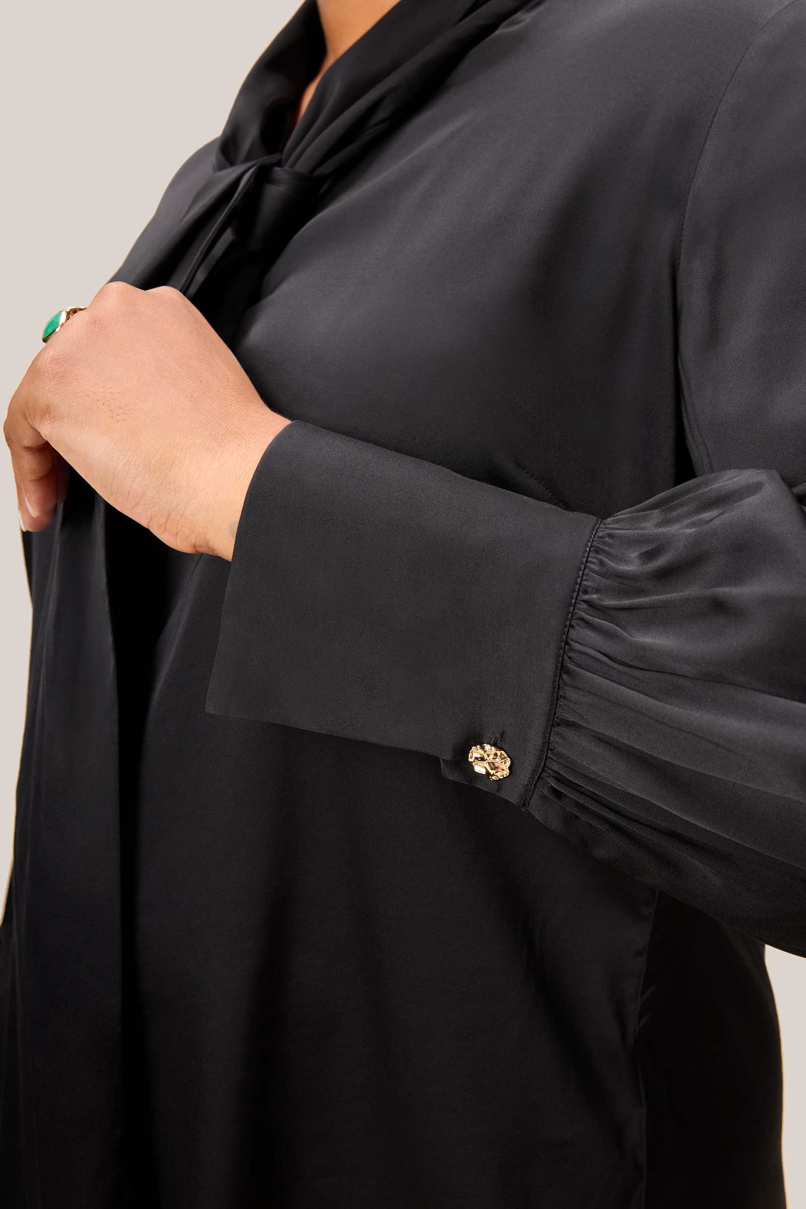 Detail shot of gold cuff buttons on black satin blouse sleeve