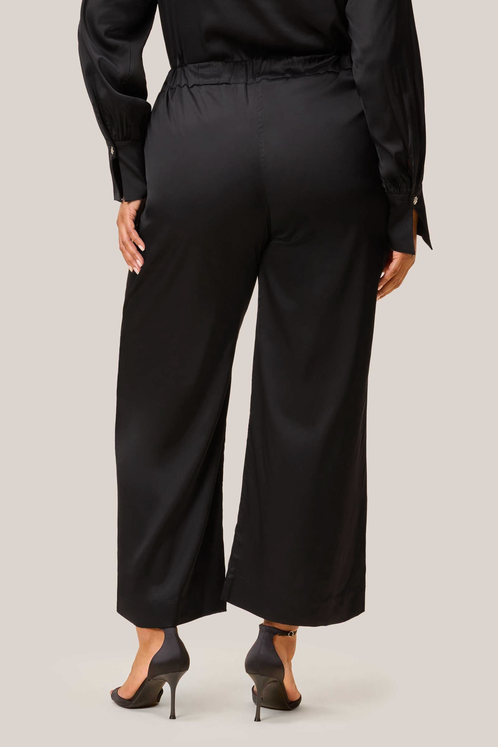 Back view of model in black satin palazzo trousers. Plus size THE HOUR