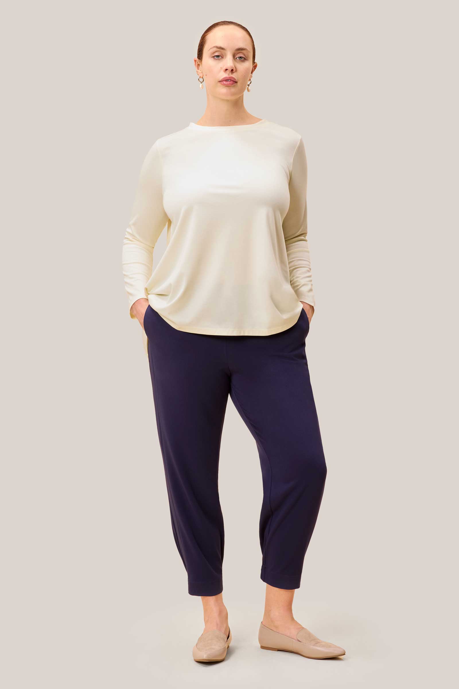 Model wearing plus size cream jersey top with long sleeves and relaxed dipped hem, styled with navy trousers.
