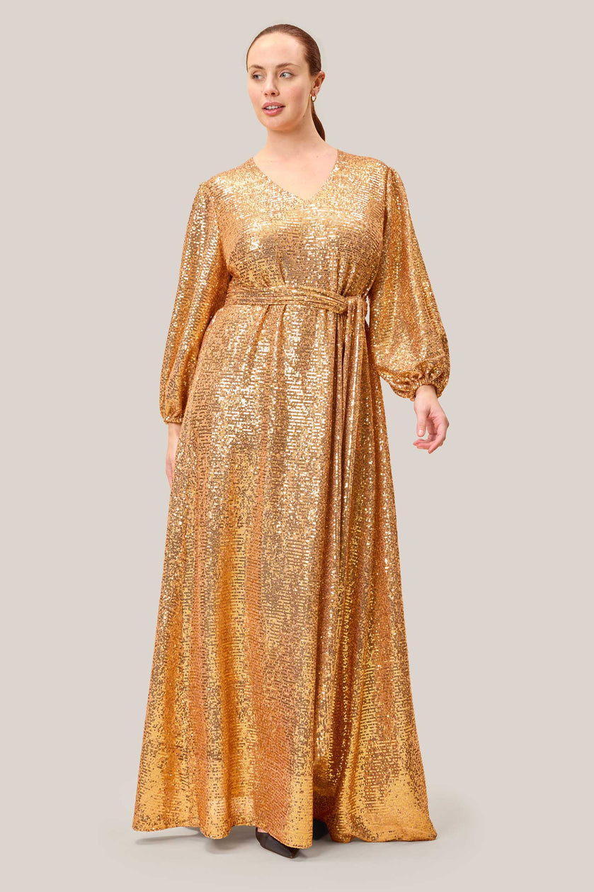 Plus-size model posing in a shimmering gold sequin maxi dress, featuring a flattering V-neck and gathered sleeves.
THE HOUR