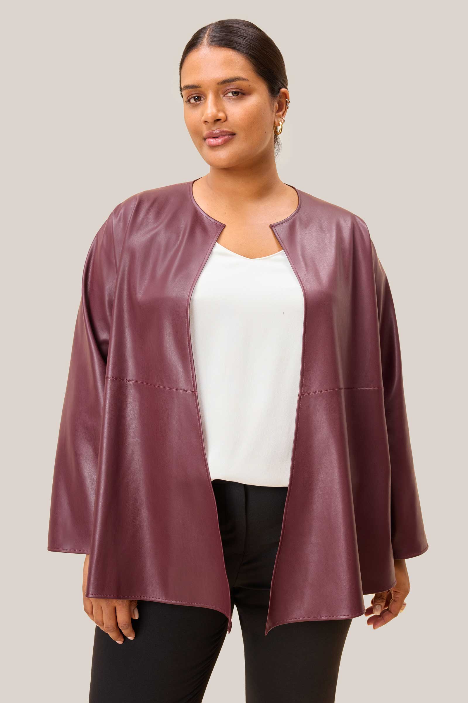 A woman wearing a burgundy leather jacket over a white top and black pants on a plain background. Plus-size - THE HOUR