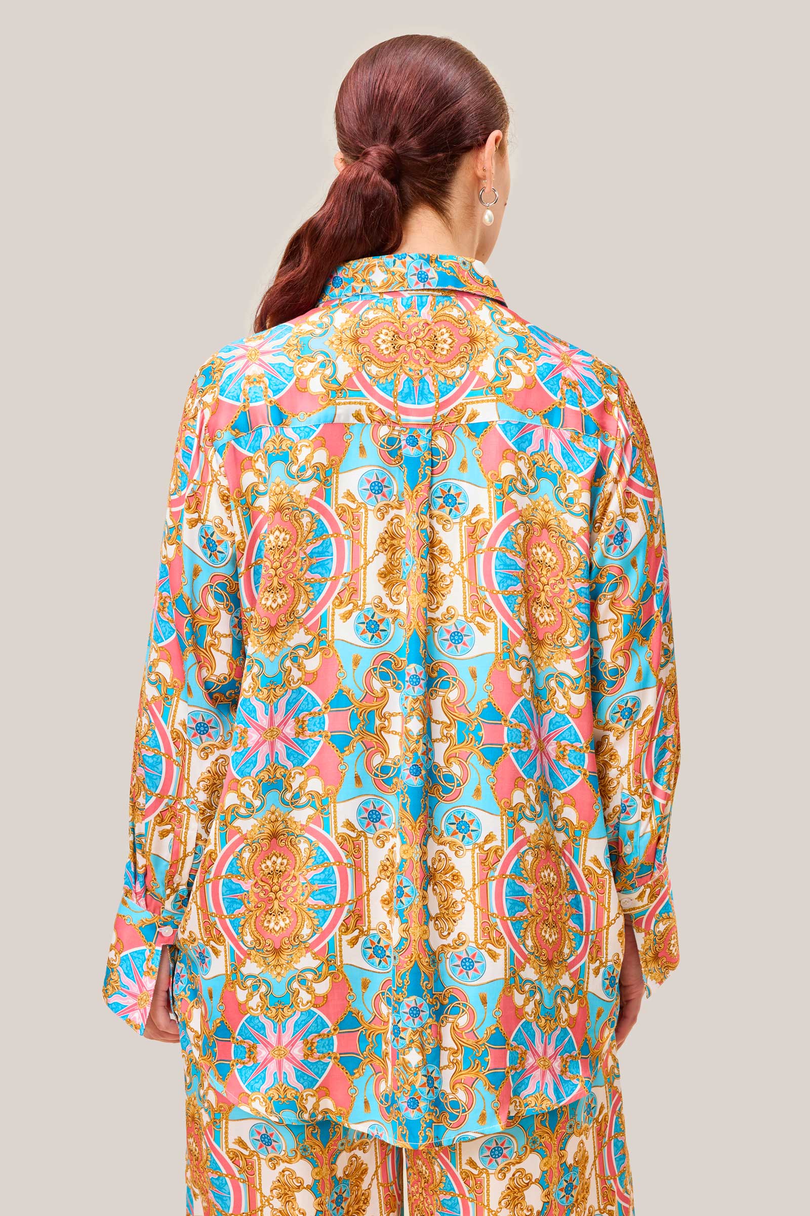 Back view of baroque print satin viscose shirt with relaxed fit and ornate coral, aqua, and gold pattern on plus size model.