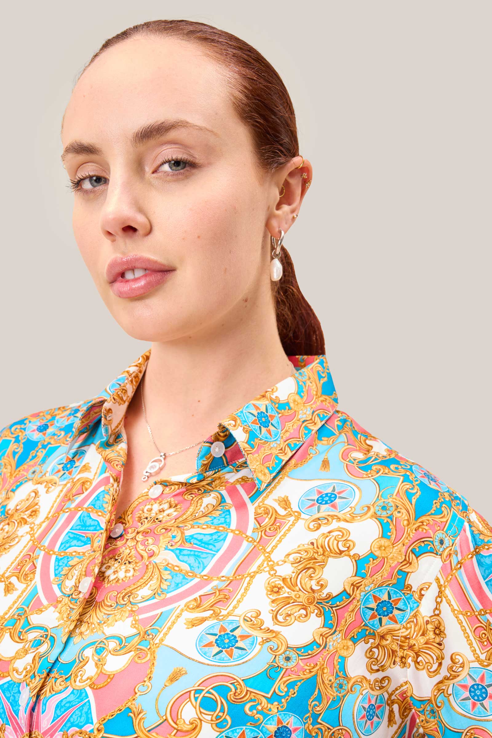 Close-up of baroque print satin shirt showing gold, pink, and turquoise pattern and concealed interior button detail for smooth bust fit.