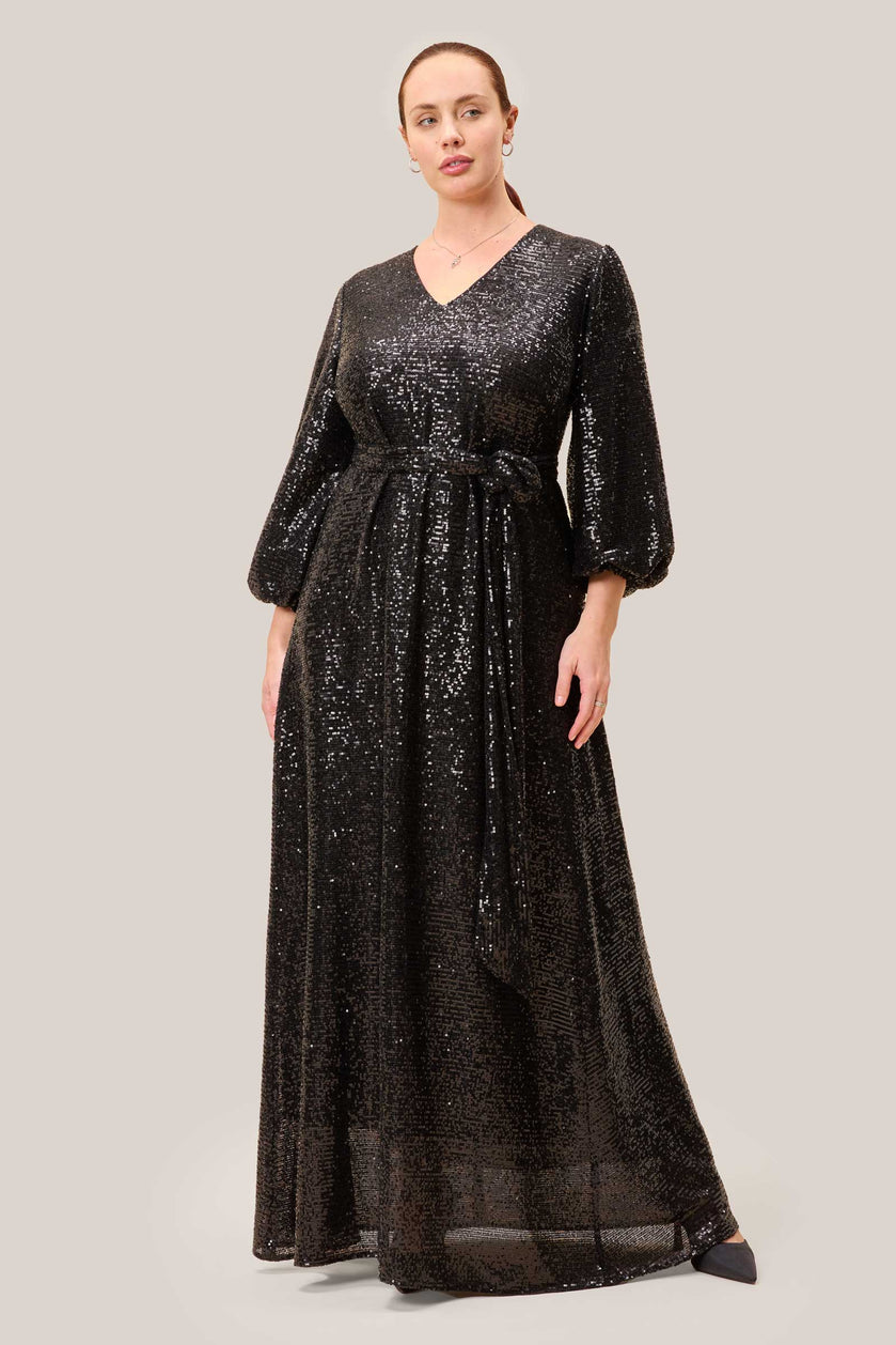 Plus-size model wearing a floor-length black sequin gown with a V-neckline and statement sleeves. THE HOUR