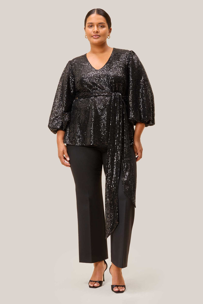 Plus-size model wearing a black sequin party blouse with long sleeves, designed by The Hour.