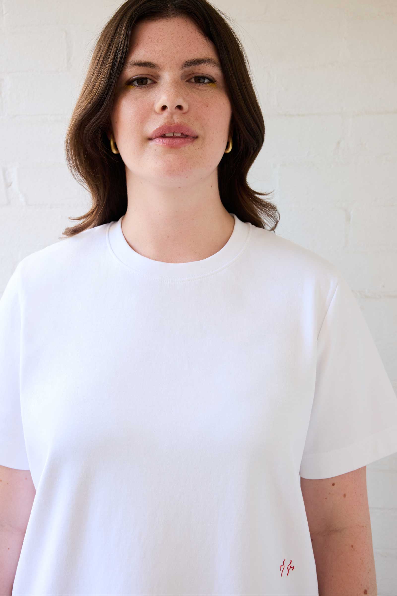 Close-up of model wearing white plus size organic cotton T-shirt with embroidered logo by The Hour