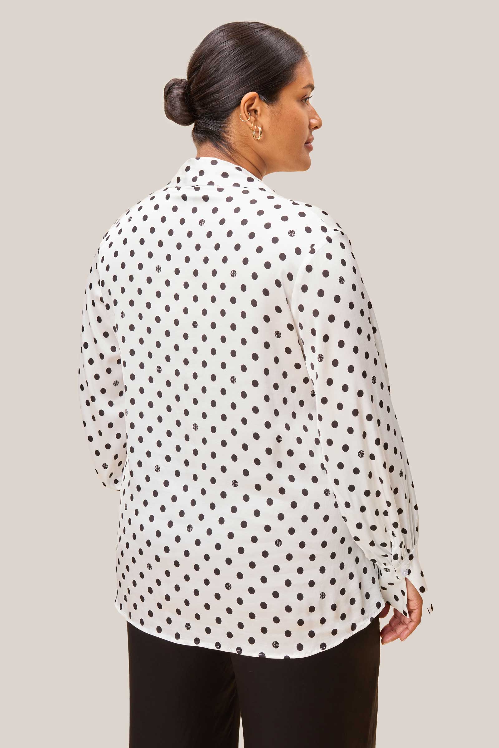 Model wearing white satin bow tie blouse with logo-detailed polka dots, back view