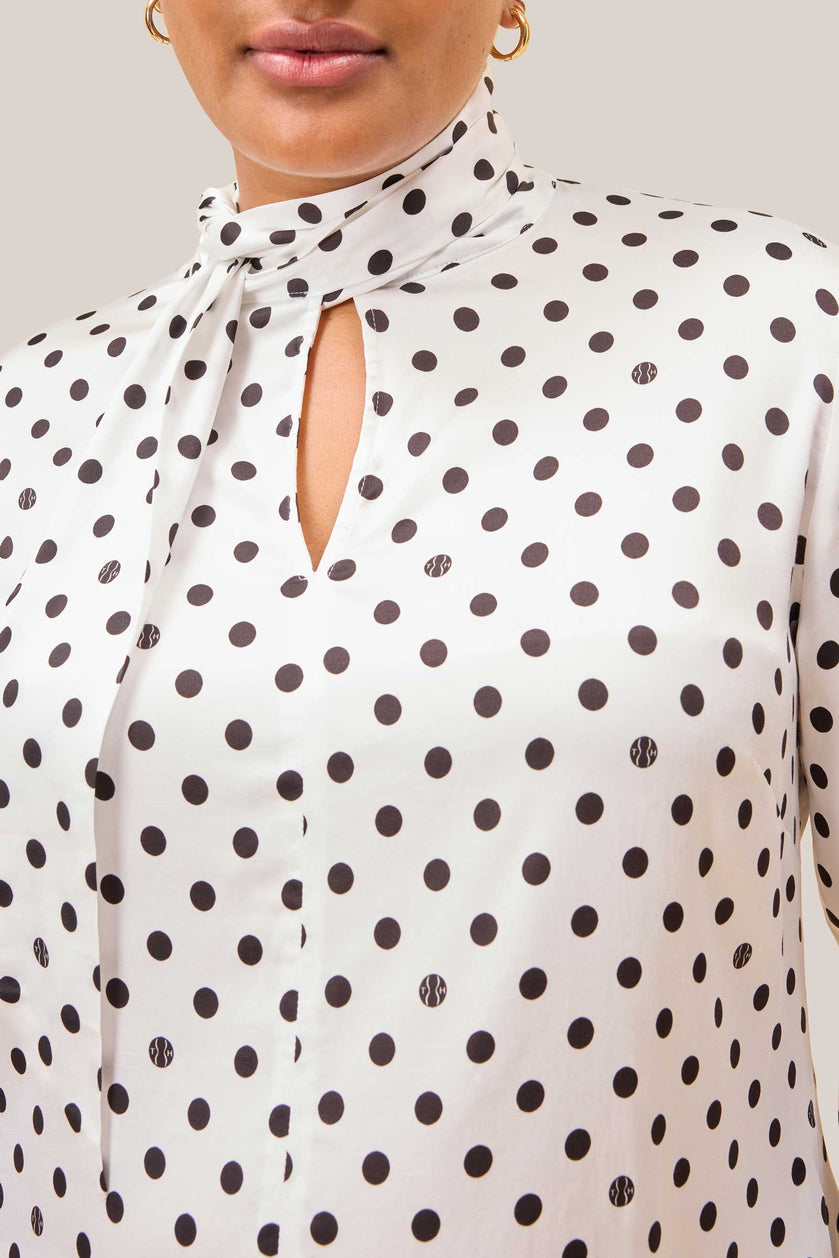Close-up of bow tie neckline and logo polka dots on white satin blouse
