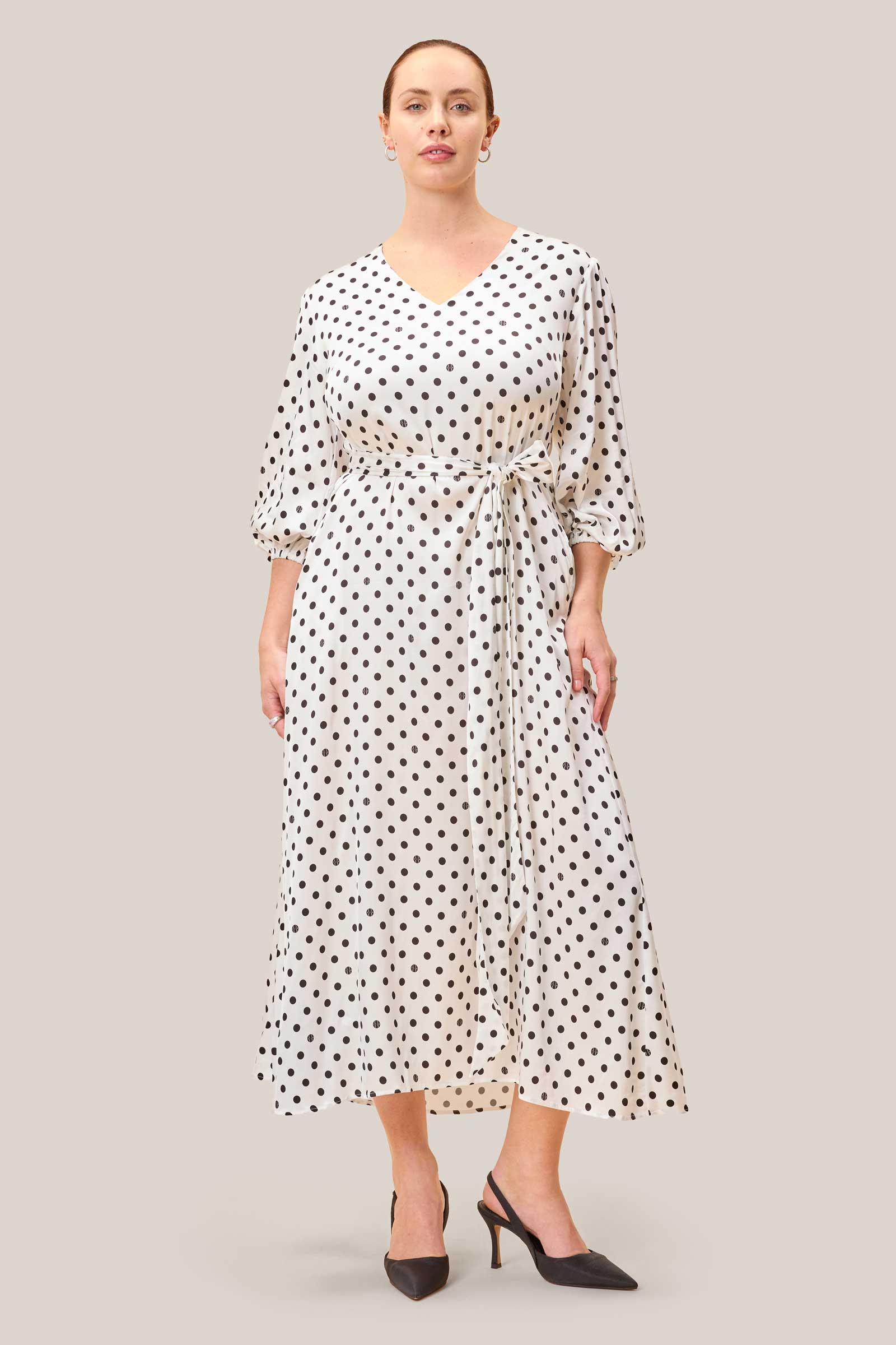 White polka dot midi dress with V-neck, belted waist and A-line silhouette, worn by model.