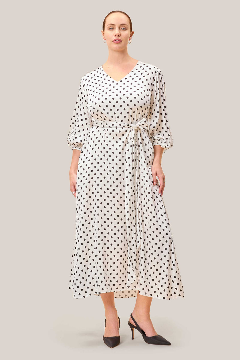 White polka dot midi dress with V-neck, belted waist and A-line silhouette, worn by model.