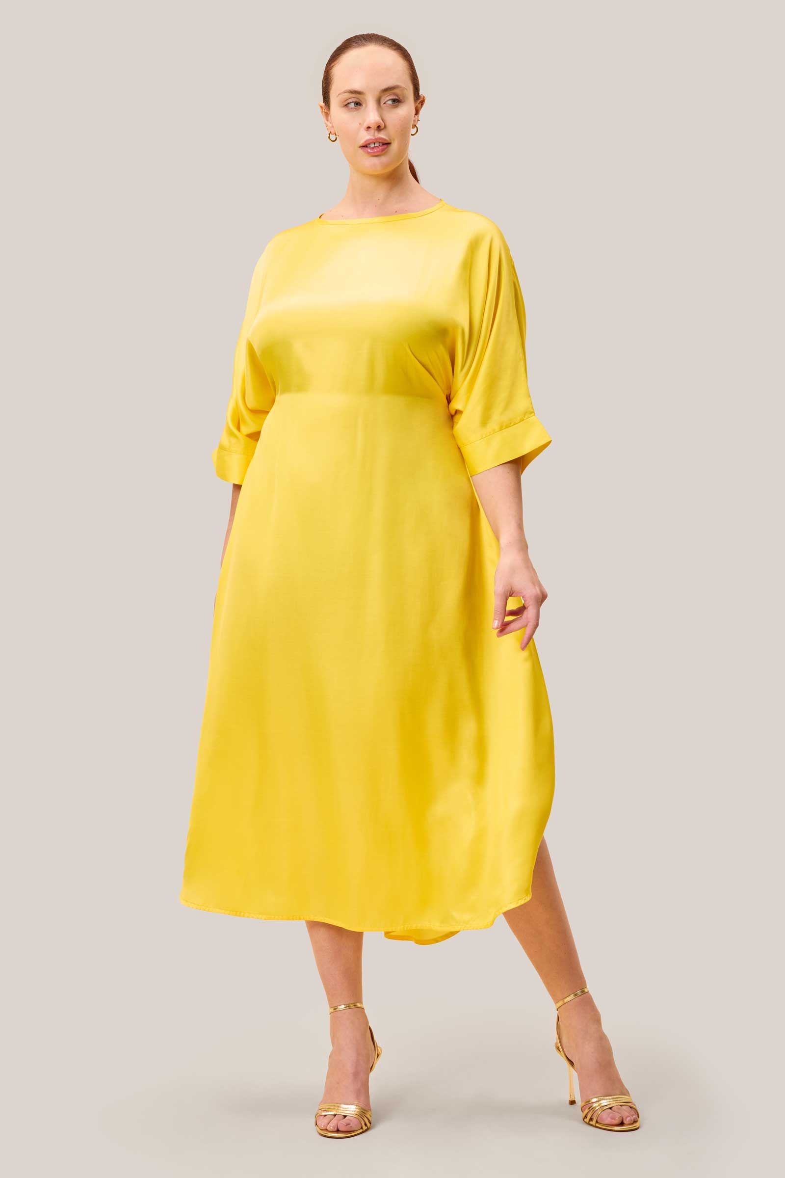 Model wearing yellow plussize satin kaftan dress with belt tied at the back. THE HOUR