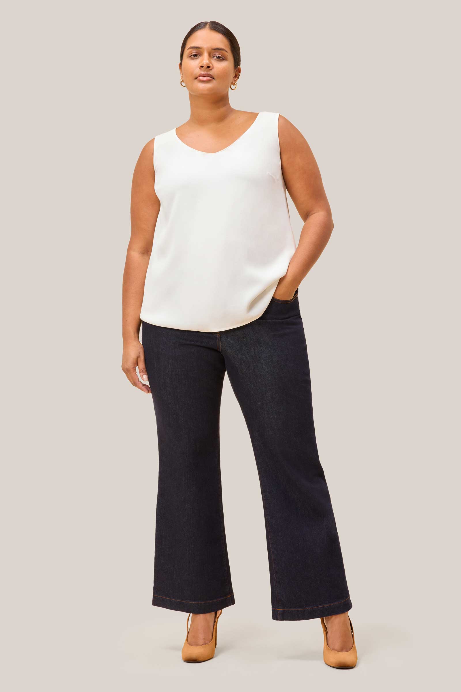 Plus size model wearing high waisted wide leg jeans in dark indigo denim and a white shell top by THE HOUR