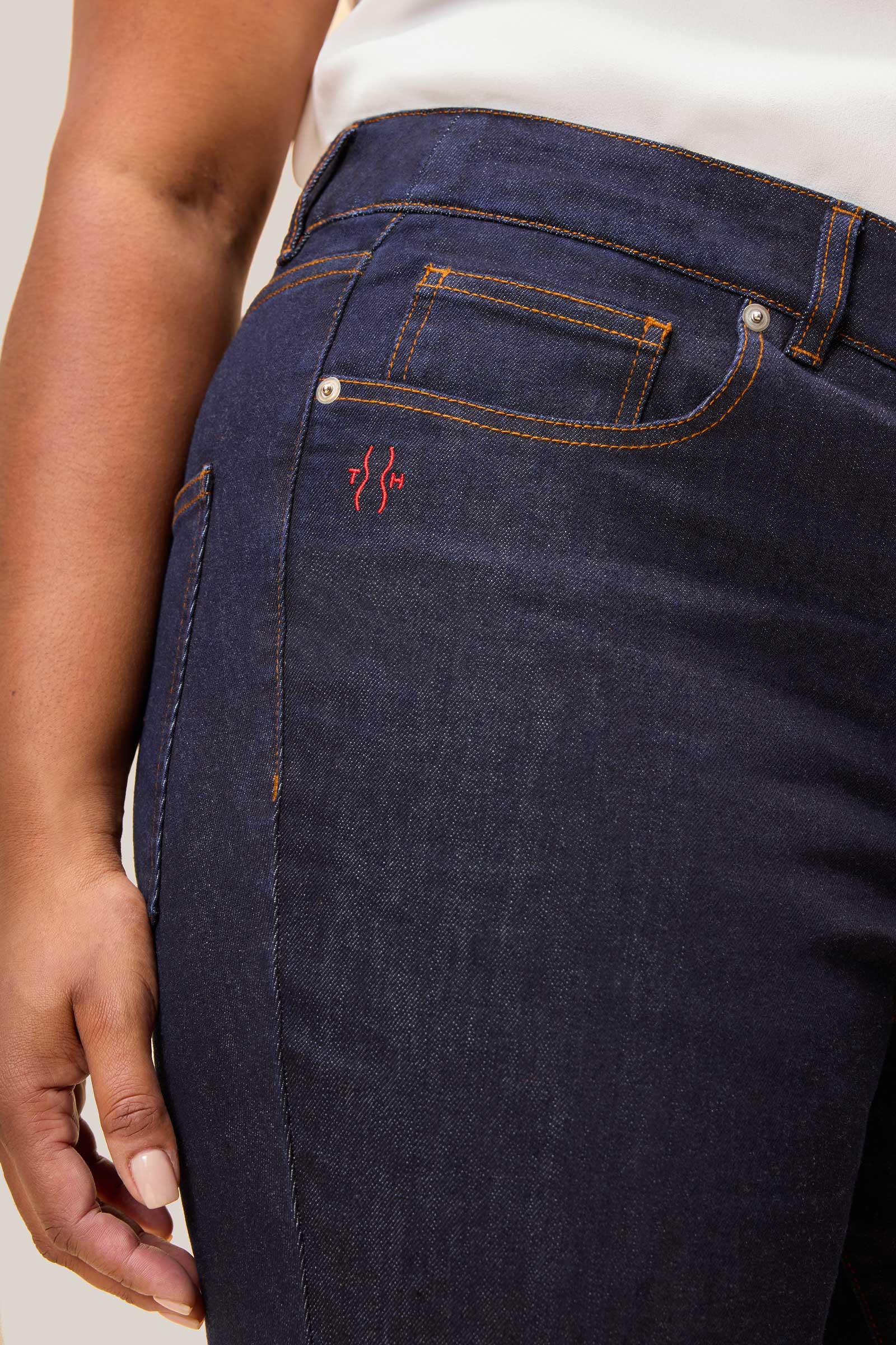 Close-up of The Hour logo red embroidery on dark indigo high waisted wide leg jeans