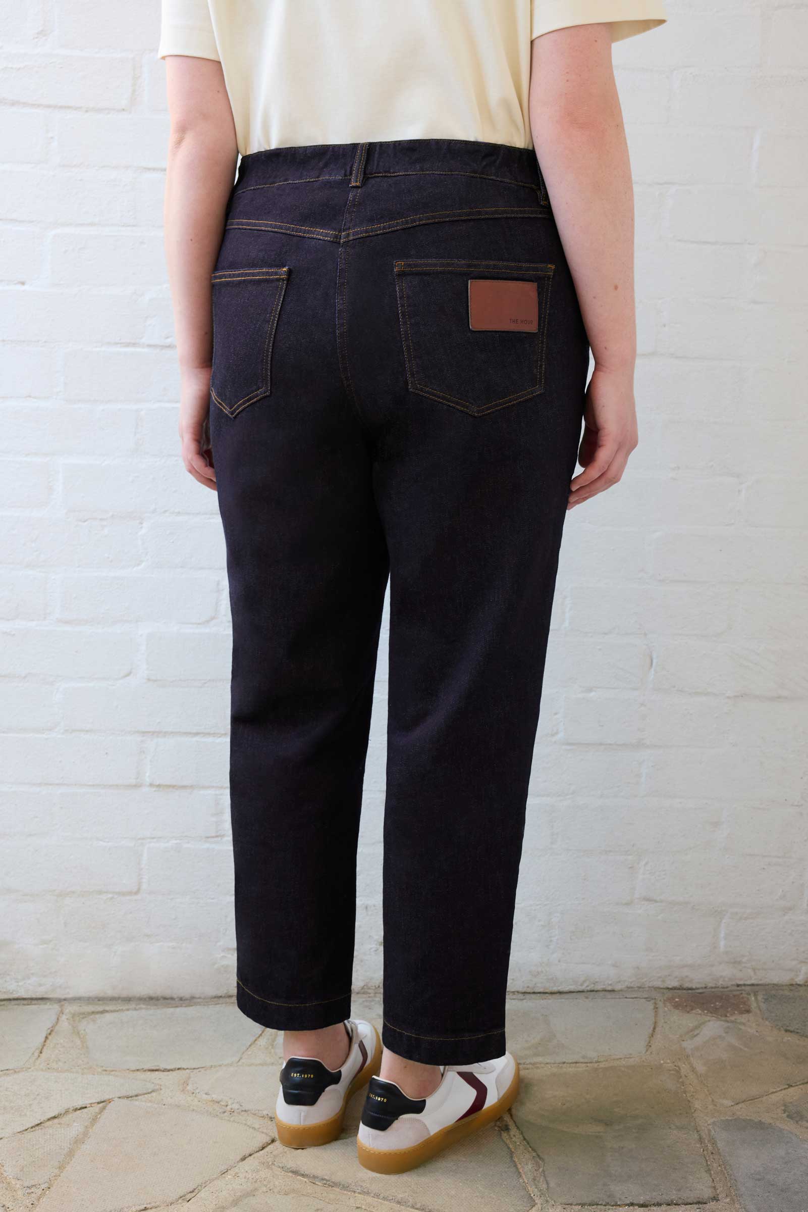 Back view of The Hour plus size tapered leg jeans in dark indigo showing logo patch