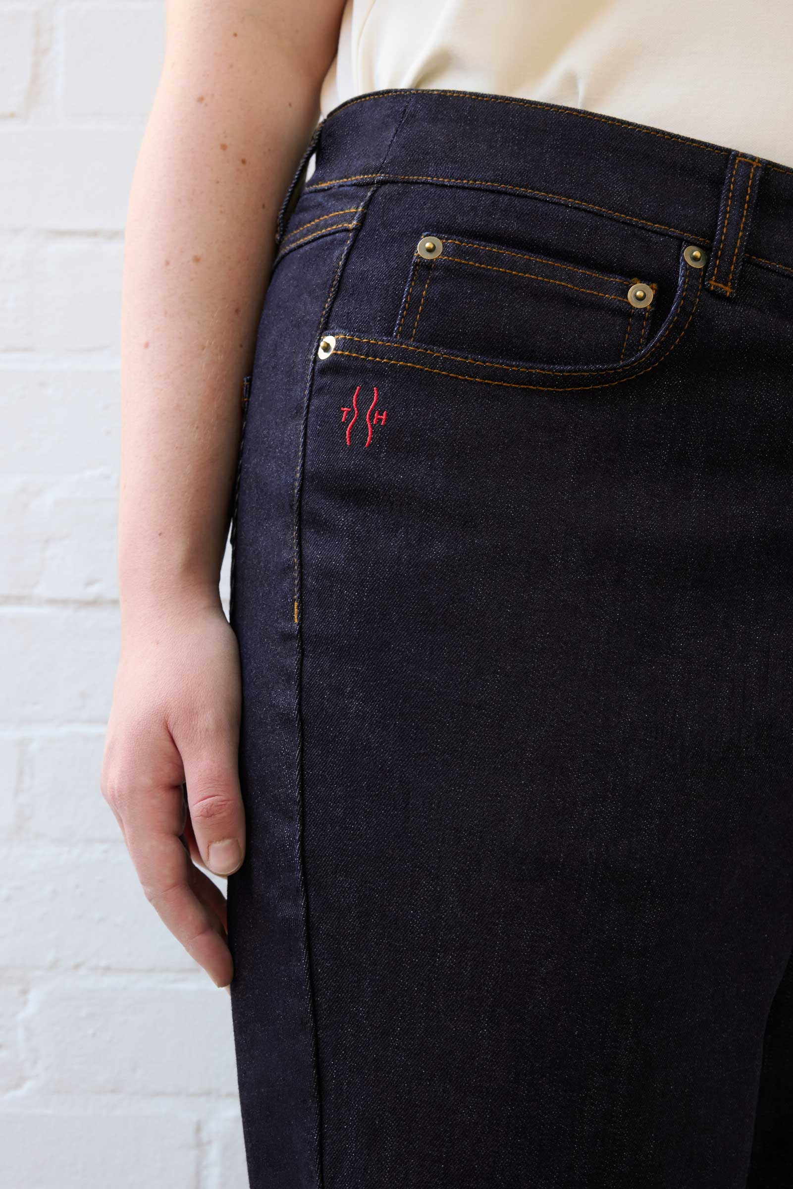 Close-up of red TH logo embroidery on The Hour plus size dark indigo jeans