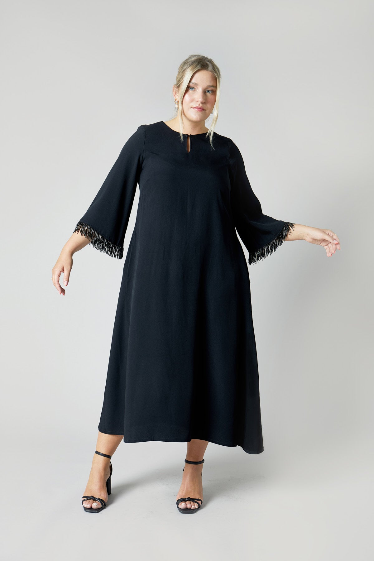 A-line black plus size maxi dress. It has wide sleeves decorated with a beaded fringe
