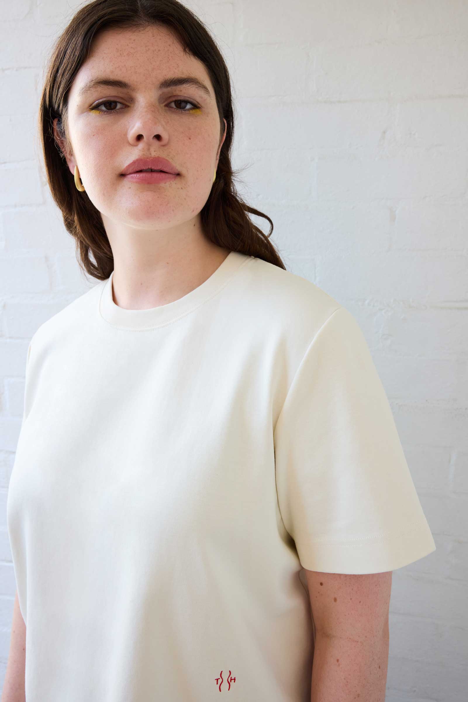 Close-up of model wearing cream plus size organic cotton T-shirt with embroidered logo by The Hour