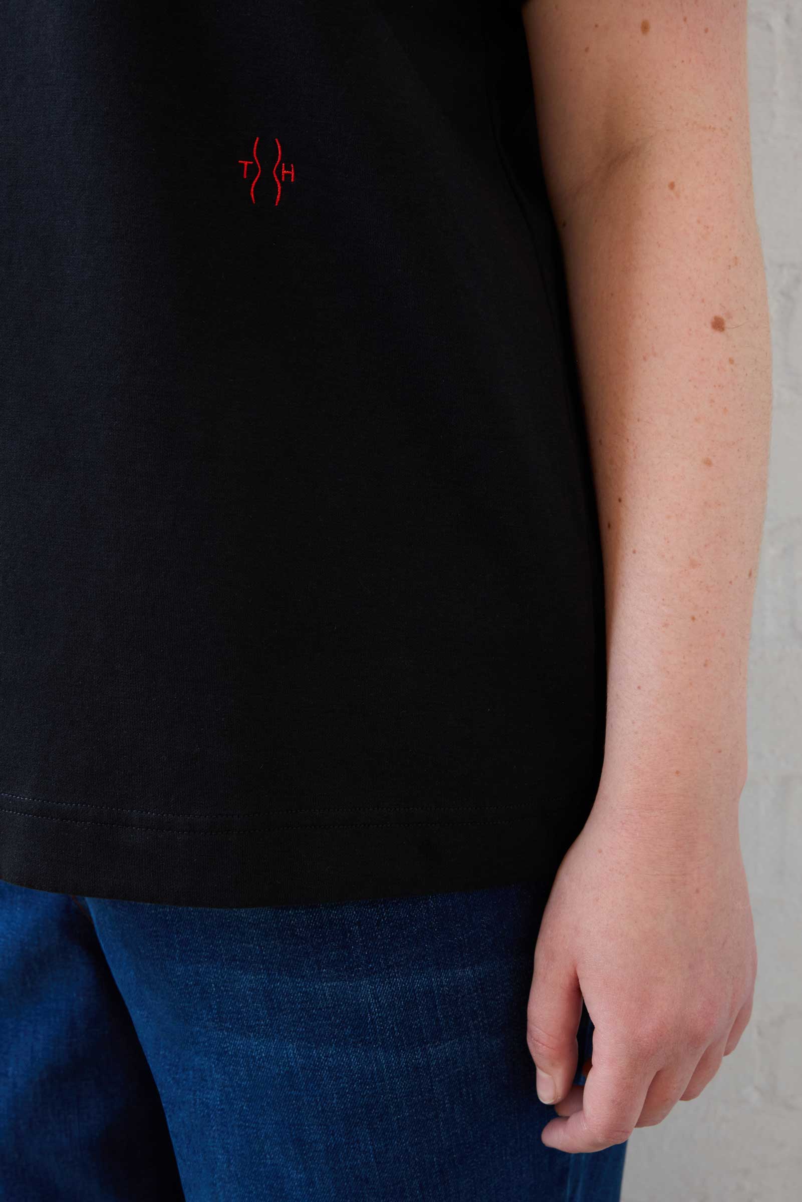 Close-up of red embroidered logo on black plus size organic cotton T-shirt by The Hour