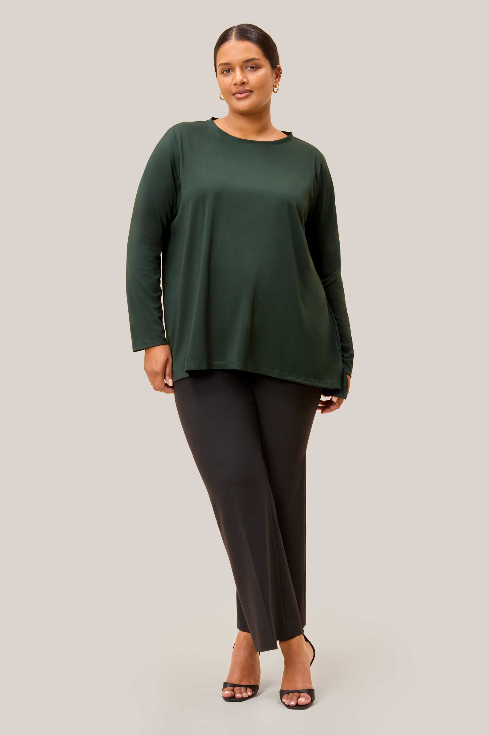 Plus size model wearing olive green jersey top with dipped hem and black trousers. THE HOUR