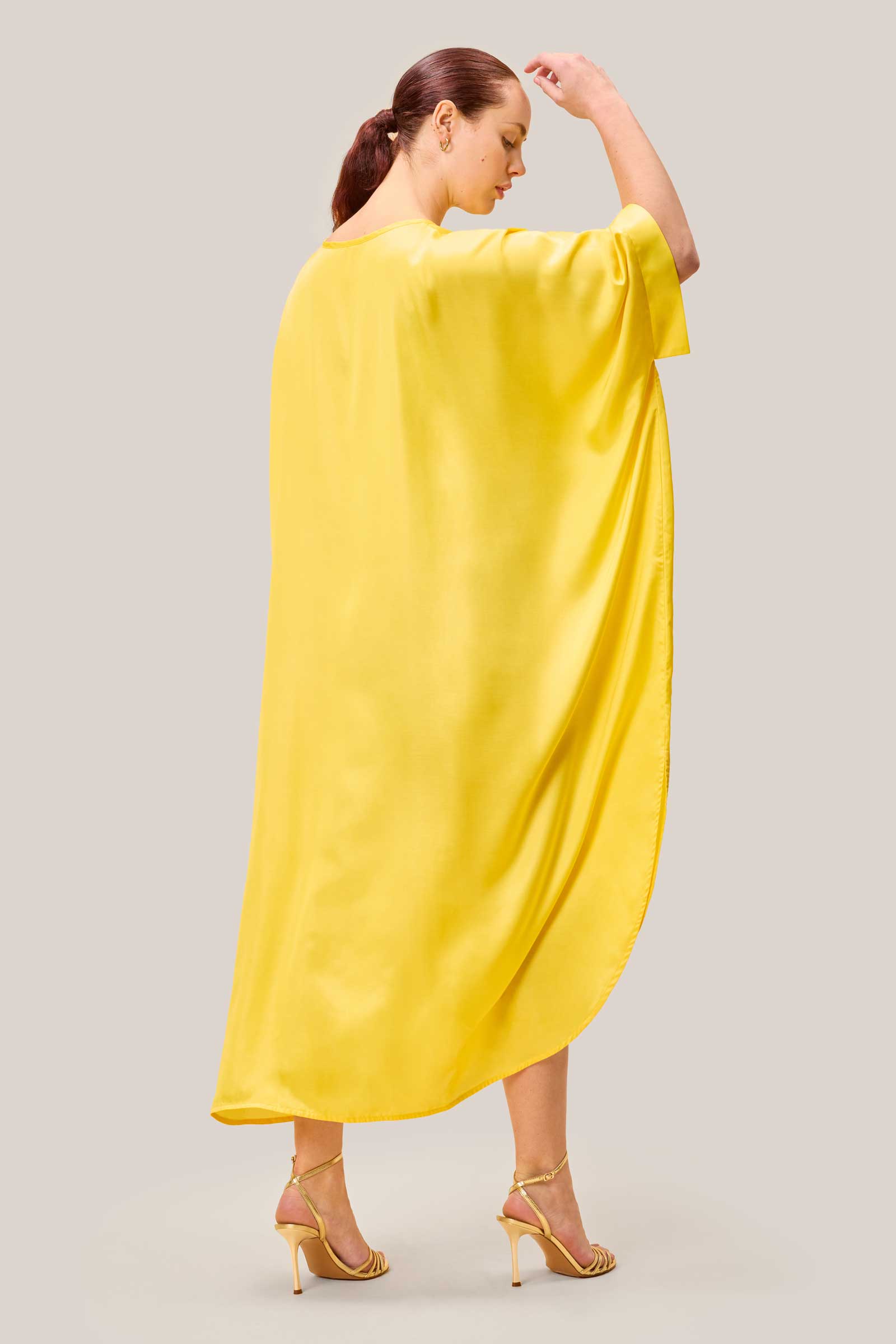 Back view of model wearing loose-fitting yellow satin plussize kaftan dress. THE HOUR HOLIDAY WEAR