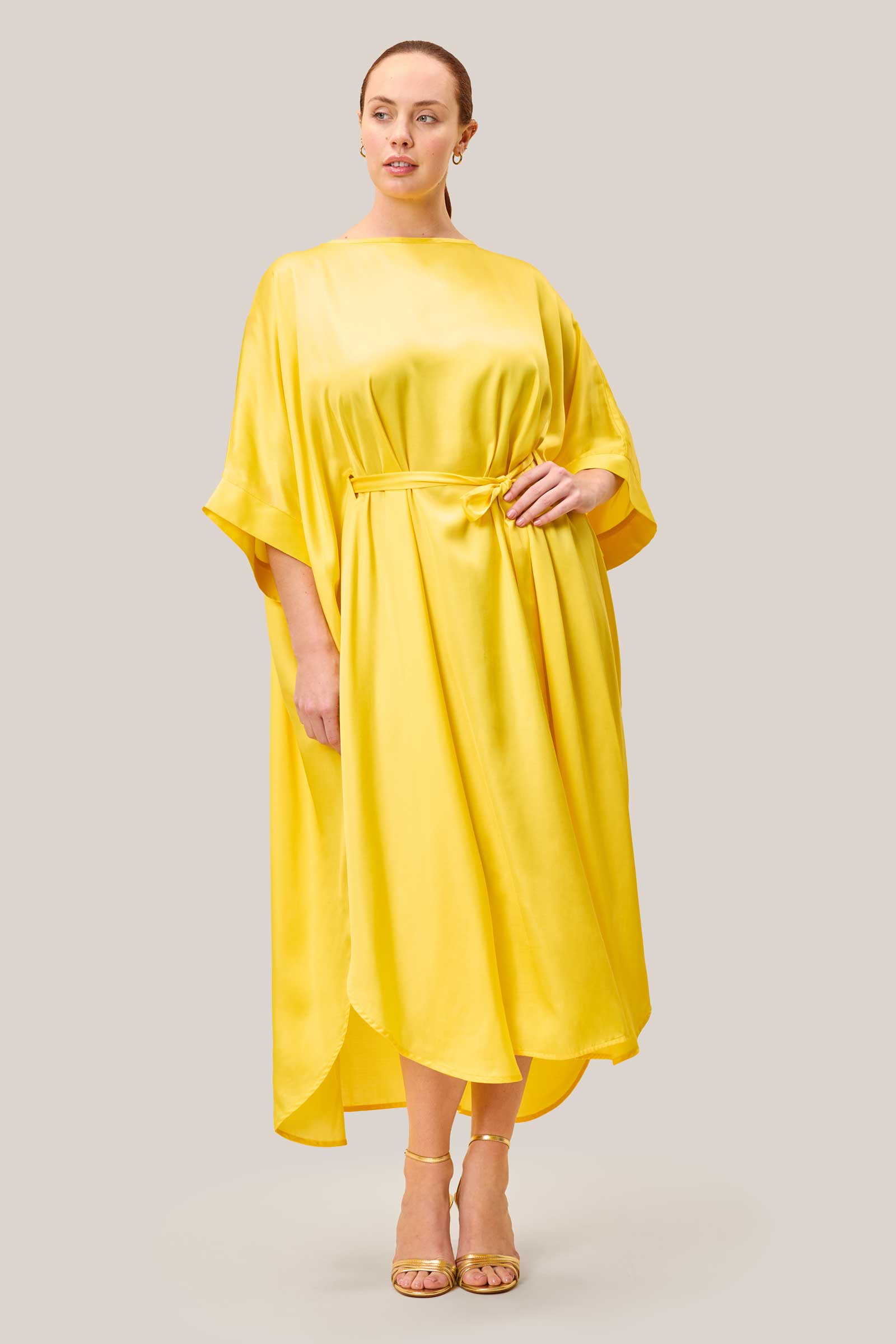 Model wearing yellow plussize satin kaftan with belt tied at the waist. THE HOUR