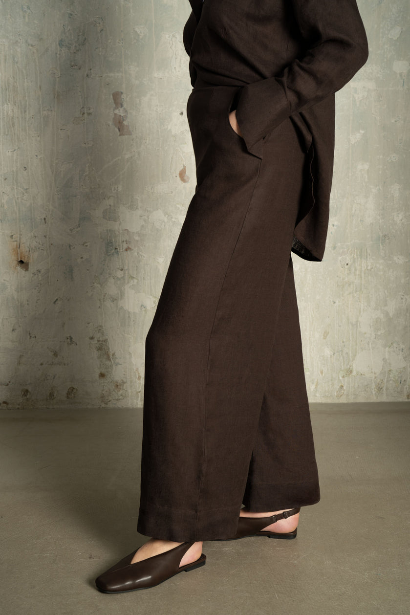 Side view of THE HOUR Chocolate Brown Linen Wide-Leg Trousers showing the relaxed fit, pocket detail and natural linen texture.