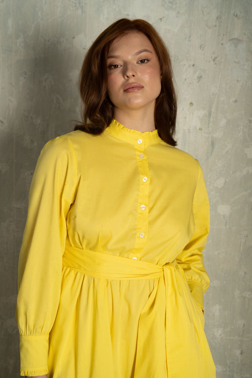 Close-up of THE HOUR's plus-size sunshine yellow Liberty cotton maxi dress, showing the ruffled mandarin collar, mother-of-pearl button placket, and self-tie waist sash